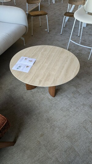 Table basse à pieds en bois et plateau rond en marbre, sur moquette grise.
